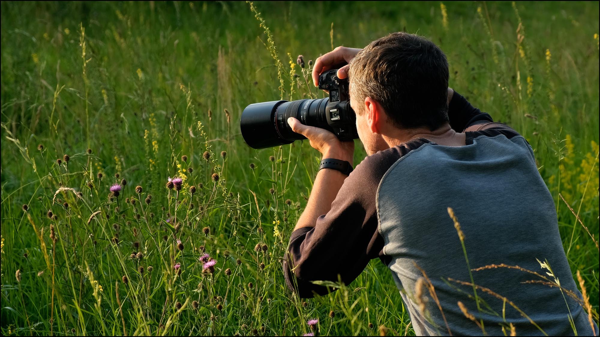 Man with camera doing macro photography of flowers in meadow