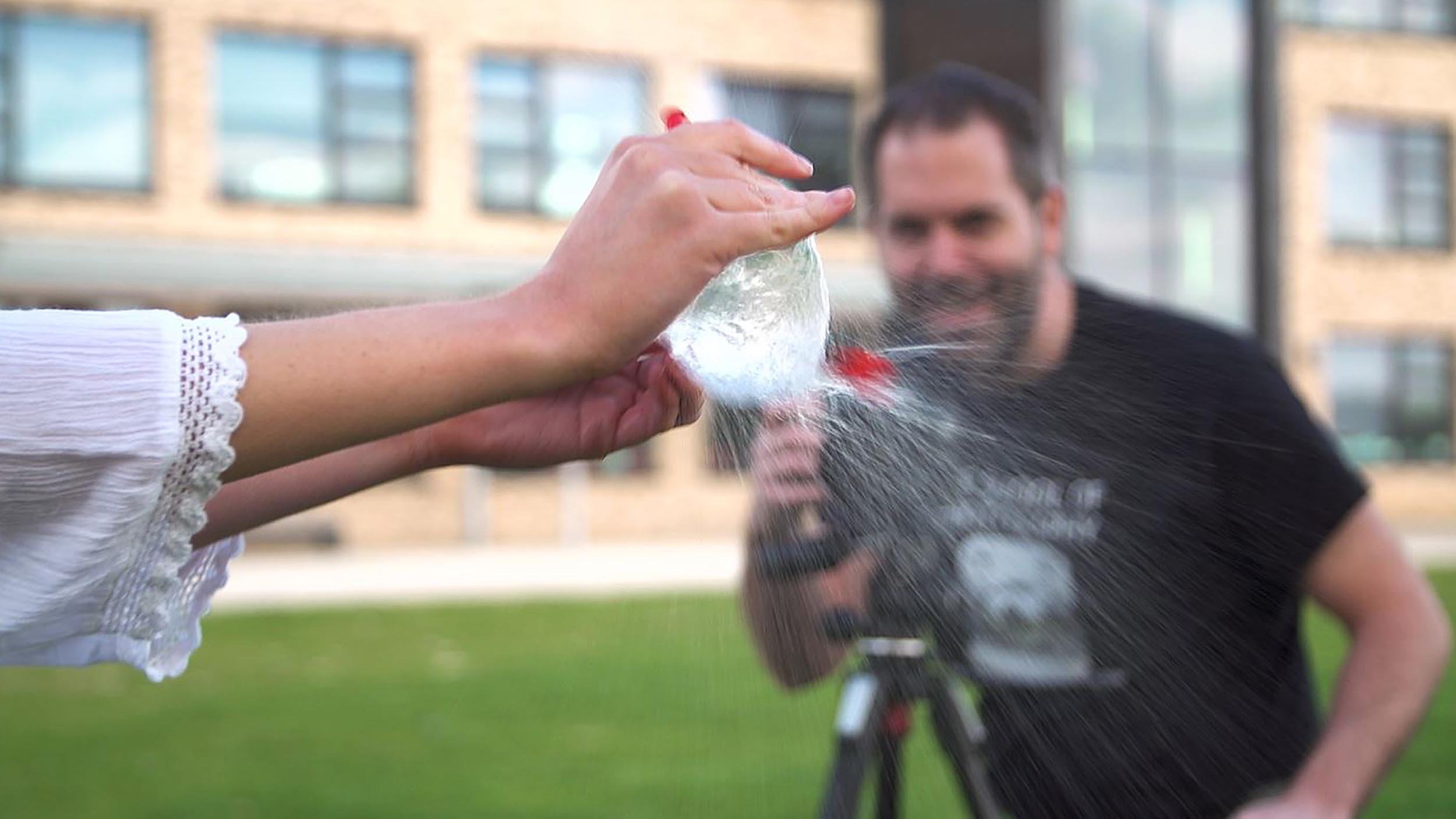 Water balloon being popped, with a person taking a photo.