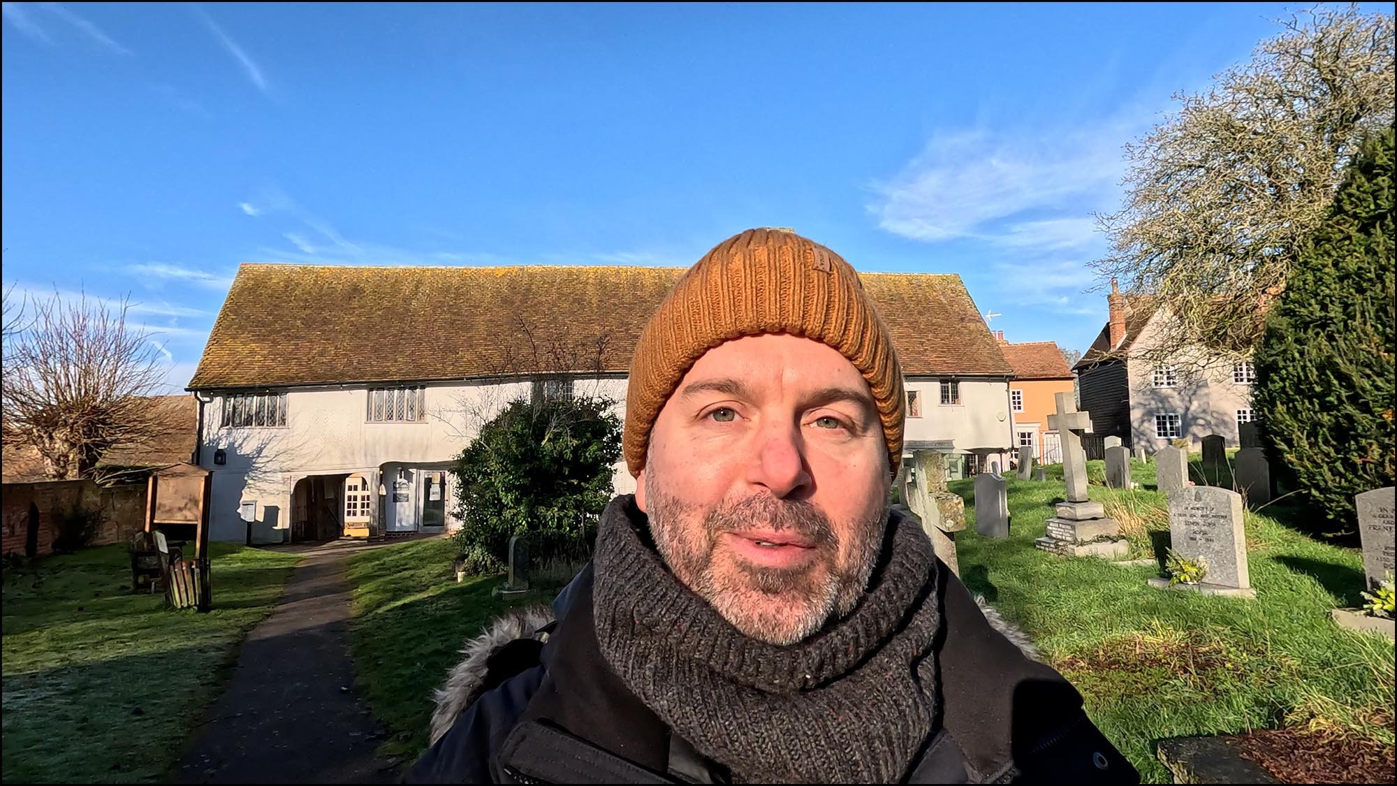 Photography instructor vlogging outdoors in a village churchyard while filming handheld video content for a videography lesson