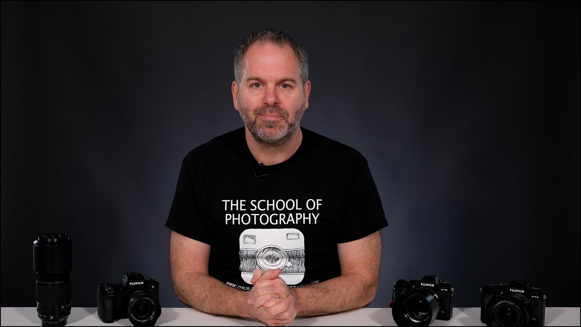 The School of Photography instructor seated at a desk with Fujifilm cameras and lenses during a videography course recap lesson