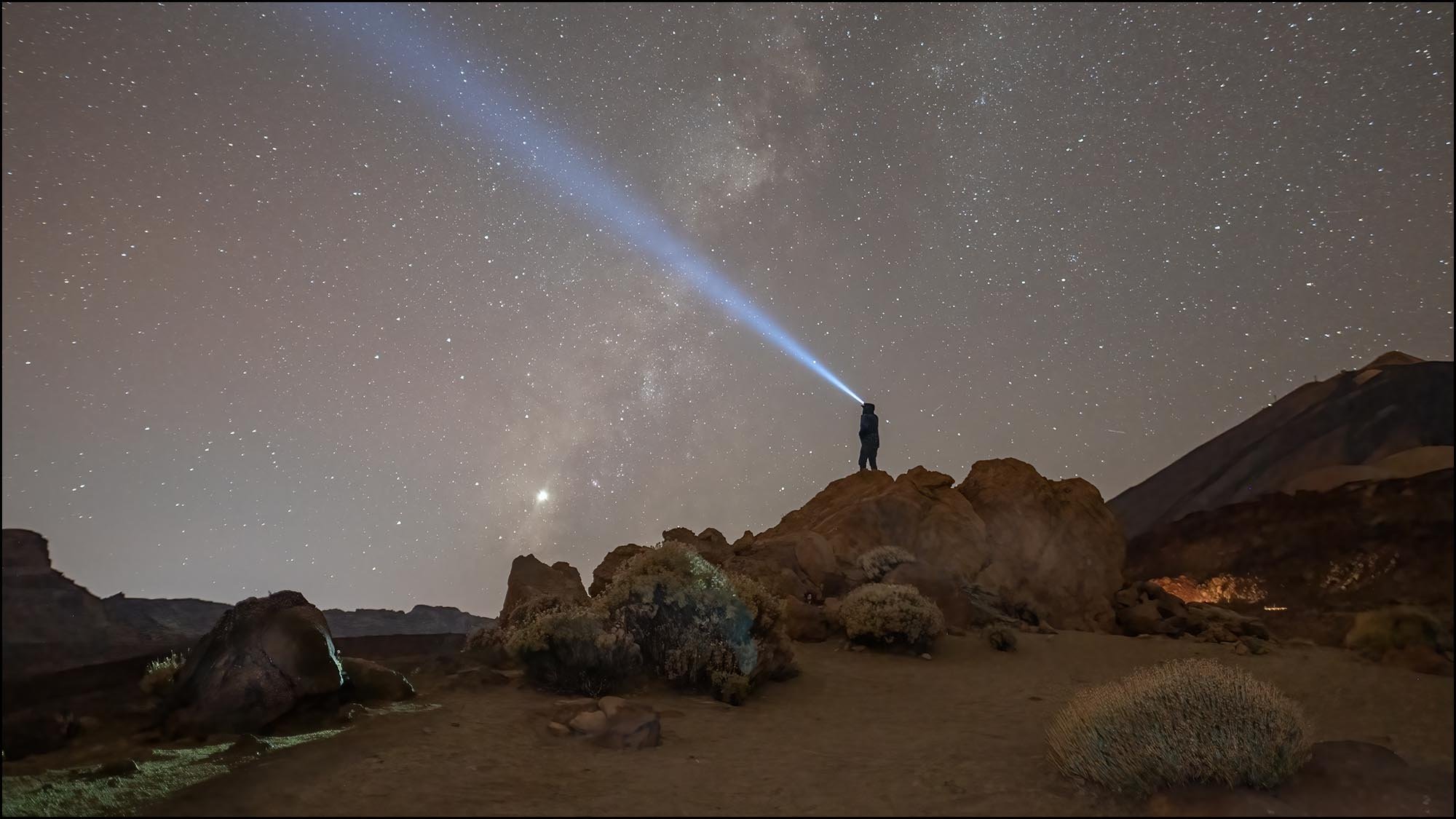 Man standing on rock with torch and Milky Way in background